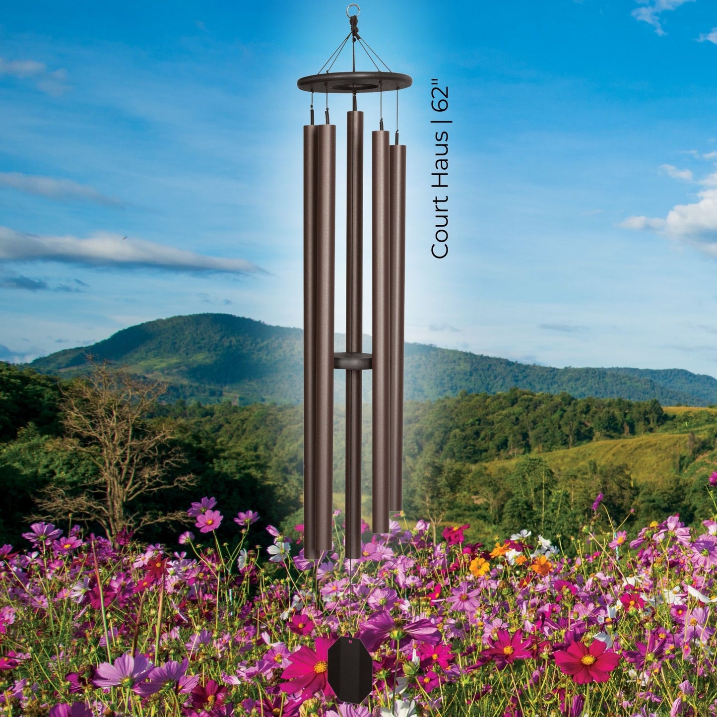 The Court Haus 62-inch handcrafted lambright bronze colored wind chime hanging over a beautiful landscape of mountains and pink flowers.