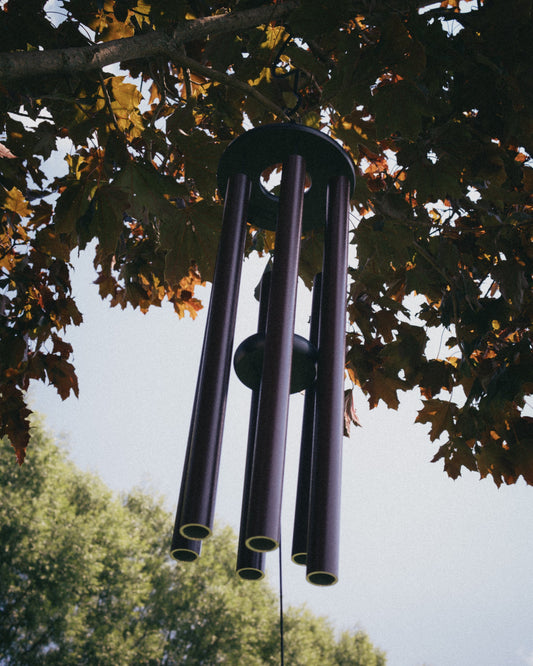 Looking up at five musically tuned aluminum wind chime tubes hanging from a round poly lumber top plate, framed by autumn maple leaves and sky