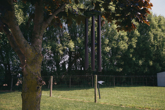 Large Amish handcrafted deep tone wind chime with dark finish hanging from a mature maple tree branch in a spacious backyard with green grass and trees