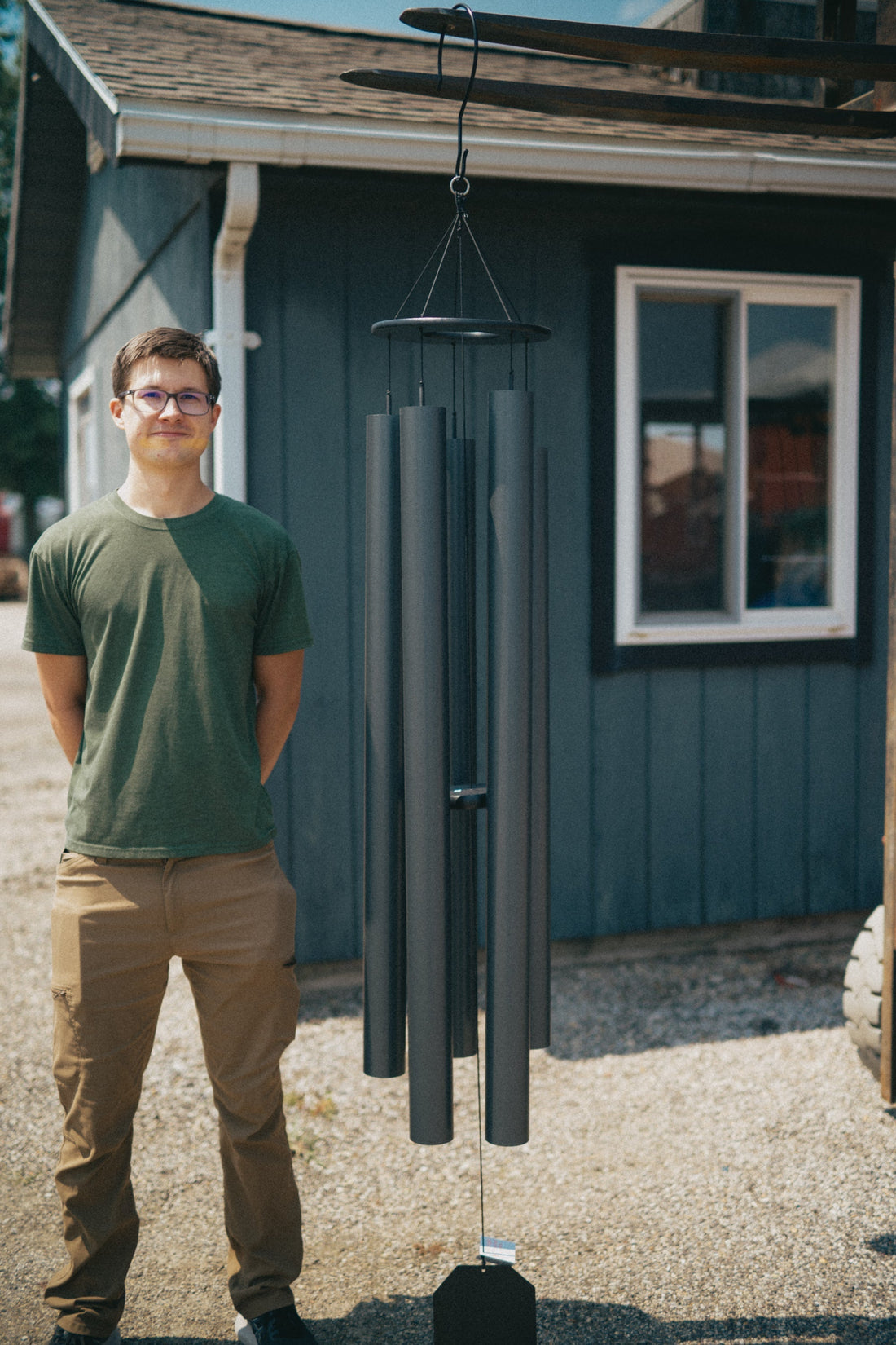 Person beside a Lambright wind chime, showing its wide aluminum tubes and hanging cords up close