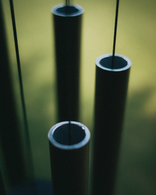 Close-up of three thick-walled powder-coated aluminum wind chime tubes from above at golden hour, showing the precision-cut rims and wall thickness