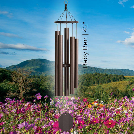 The Baby Ben 42-inch handcrafted lambright bronze colored wind chime hanging over a beautiful landscape of mountains and pink flowers. #42" - Baby Ben
