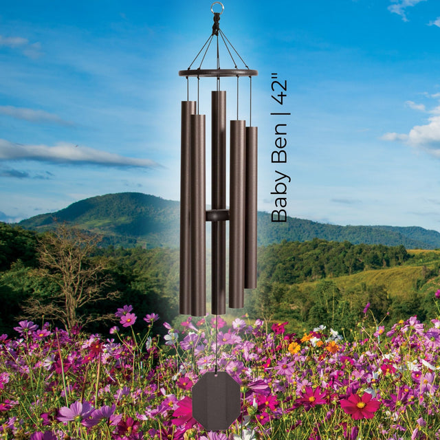 The Baby Ben 42-inch handcrafted lambright bronze colored wind chime hanging over a beautiful landscape of mountains and pink flowers. #42" - Baby Ben